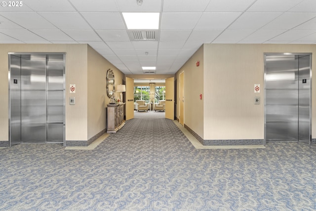 hallway featuring dark colored carpet, a paneled ceiling, and elevator