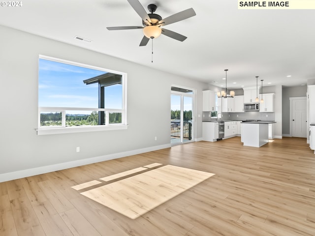 unfurnished living room featuring a wealth of natural light, sink, light hardwood / wood-style floors, and ceiling fan with notable chandelier