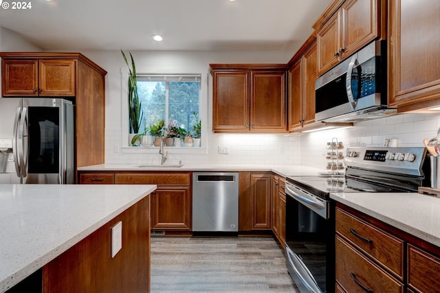 kitchen with tasteful backsplash, sink, stainless steel appliances, and light wood-type flooring