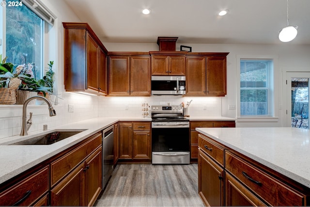 kitchen featuring appliances with stainless steel finishes, light stone counters, sink, decorative light fixtures, and light hardwood / wood-style floors