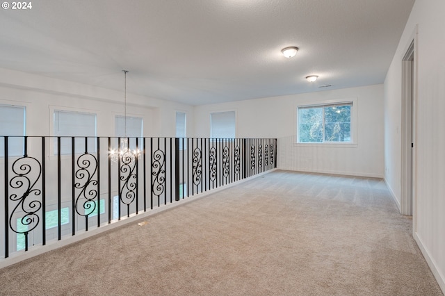 spare room with light carpet, a textured ceiling, and a chandelier