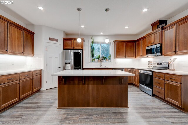 kitchen featuring stainless steel appliances, hanging light fixtures, and light hardwood / wood-style flooring