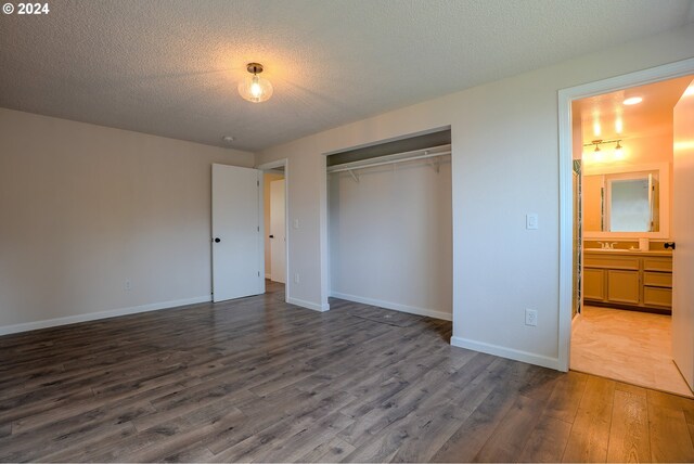 unfurnished bedroom featuring connected bathroom, sink, dark hardwood / wood-style floors, a textured ceiling, and a closet