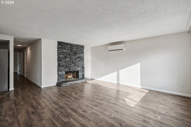 unfurnished living room featuring a wall mounted AC, dark hardwood / wood-style flooring, a fireplace, and a textured ceiling