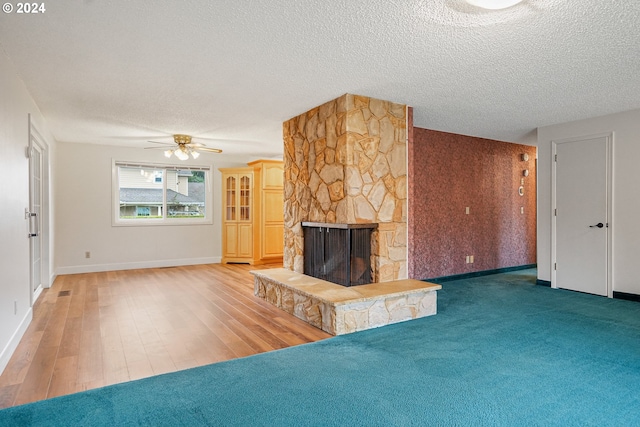 unfurnished living room featuring ceiling fan, a fireplace, wood-type flooring, and a textured ceiling