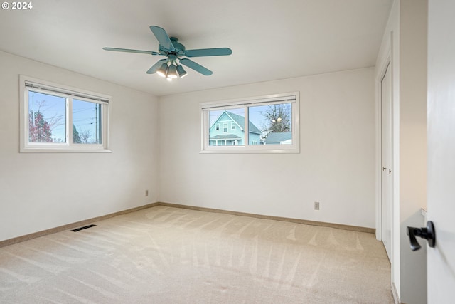 spare room with light colored carpet, a wealth of natural light, and ceiling fan