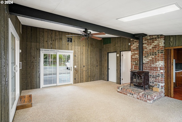 unfurnished living room featuring beamed ceiling, carpet flooring, a wood stove, and wooden walls