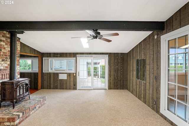 living room featuring a wood stove, wood walls, a healthy amount of sunlight, and vaulted ceiling with beams