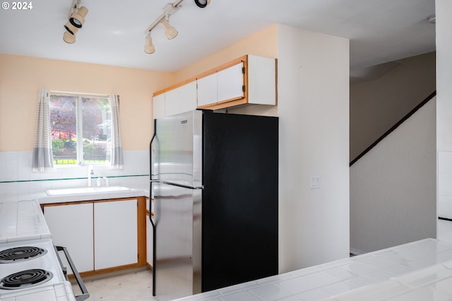 kitchen featuring tile counters, track lighting, stainless steel refrigerator, white cabinetry, and sink