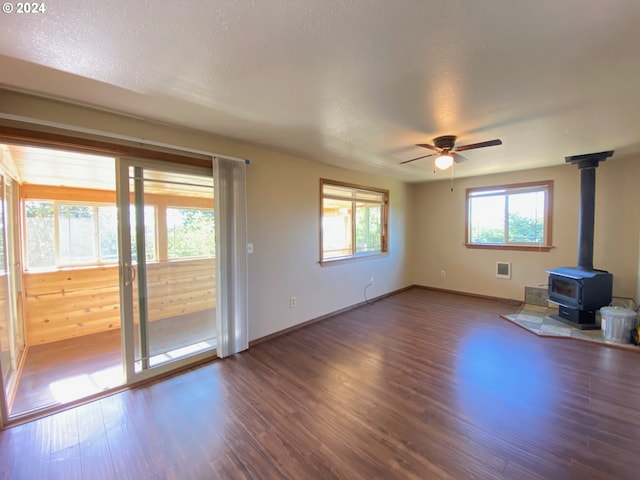 unfurnished living room with a textured ceiling, wood-type flooring, a wood stove, and ceiling fan