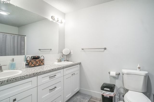 bathroom featuring tasteful backsplash, a textured ceiling, toilet, and dual vanity