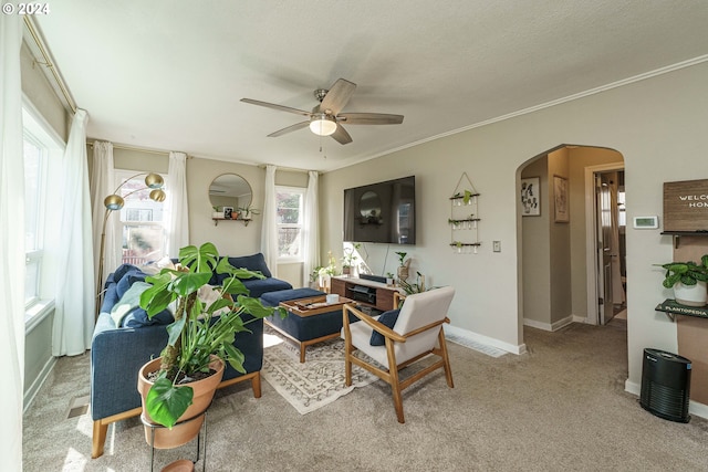 living area with baseboards, arched walkways, a ceiling fan, light colored carpet, and crown molding