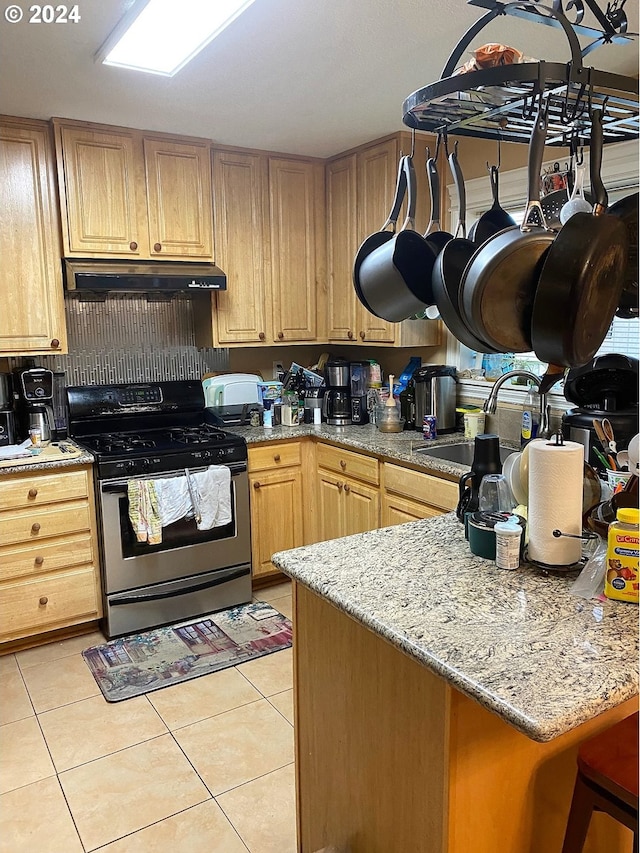 kitchen with light brown cabinetry, sink, light stone counters, stainless steel gas stove, and light tile patterned flooring