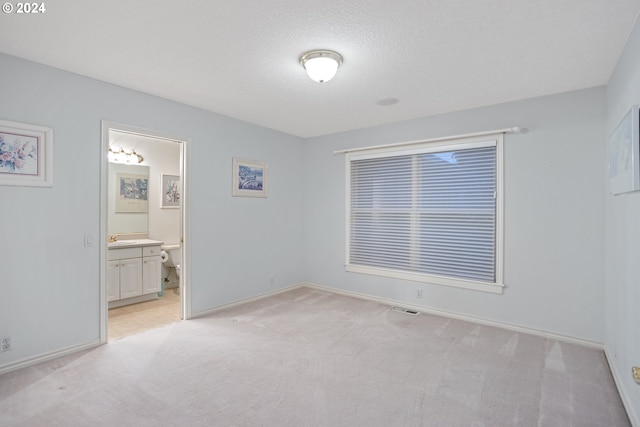 unfurnished bedroom with light carpet, a textured ceiling, connected bathroom, and sink