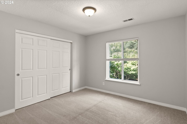 unfurnished bedroom featuring a textured ceiling, a closet, and light colored carpet