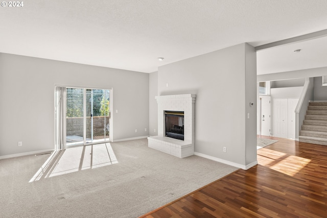 unfurnished living room with a textured ceiling, a brick fireplace, and hardwood / wood-style floors