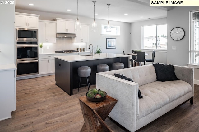 kitchen featuring pendant lighting, built in microwave, a kitchen island with sink, and white cabinets