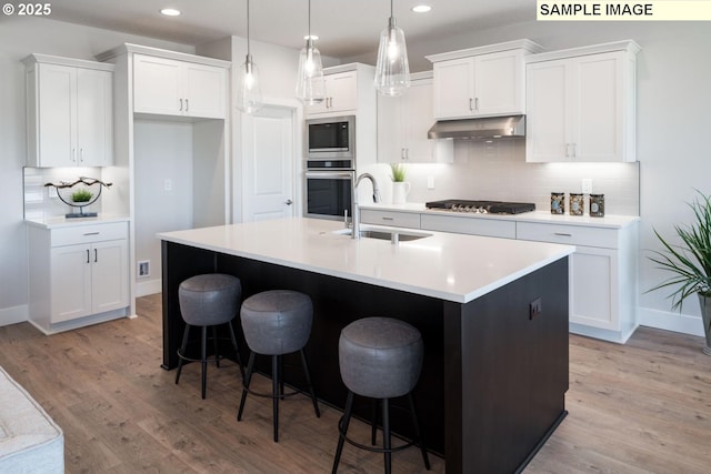 kitchen with an island with sink, stainless steel appliances, sink, and white cabinets