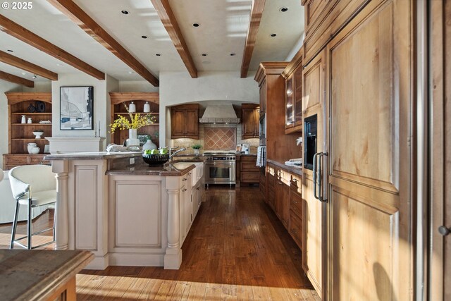 kitchen featuring premium range hood, a kitchen island, wood-type flooring, high end stove, and a kitchen bar