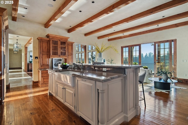 kitchen featuring dark hardwood / wood-style floors, beamed ceiling, a kitchen breakfast bar, a center island with sink, and french doors