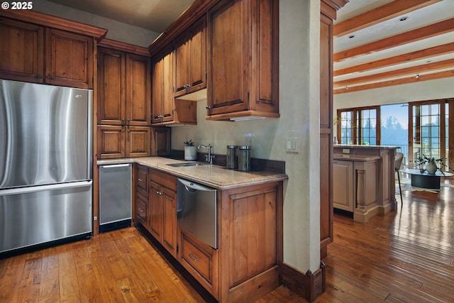 kitchen with sink, light stone counters, appliances with stainless steel finishes, beam ceiling, and hardwood / wood-style floors