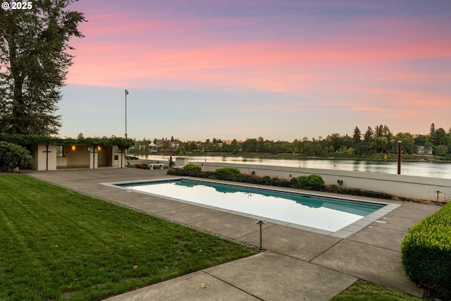 pool at dusk featuring a water view, a patio area, an outdoor structure, and a lawn