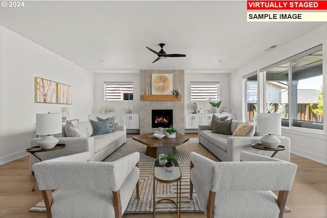 living room with light wood-type flooring, a tiled fireplace, ceiling fan, and a wealth of natural light