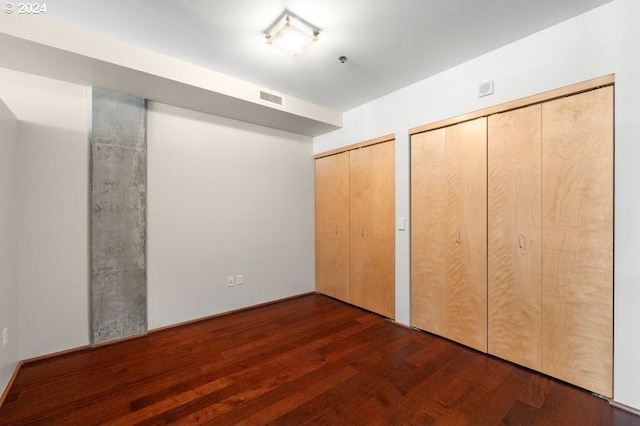 unfurnished bedroom with two closets and dark wood-type flooring