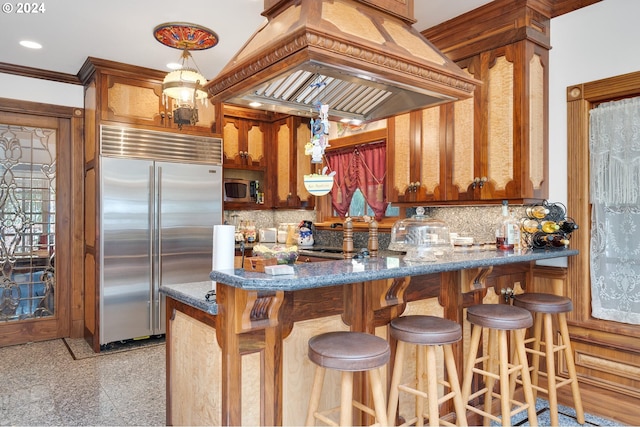 kitchen with stainless steel appliances, premium range hood, kitchen peninsula, crown molding, and dark stone countertops