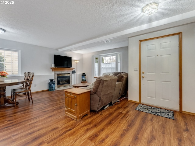 living area featuring a textured ceiling, wood finished floors, baseboards, and a tile fireplace