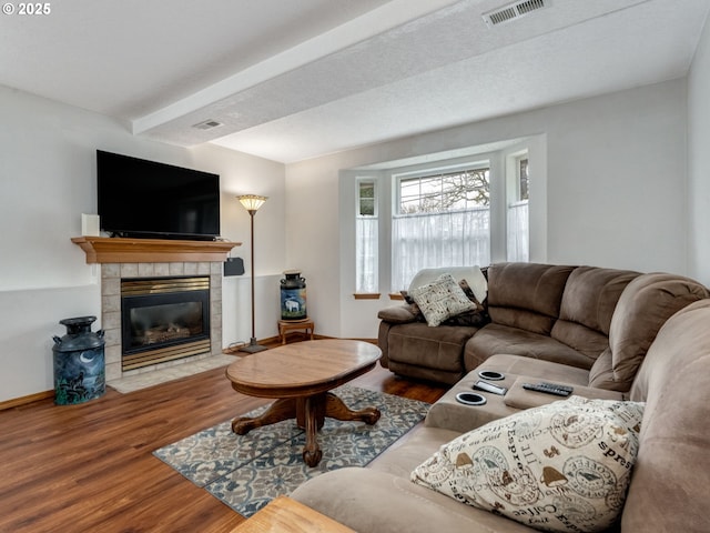 living area featuring visible vents, a tile fireplace, baseboards, and wood finished floors