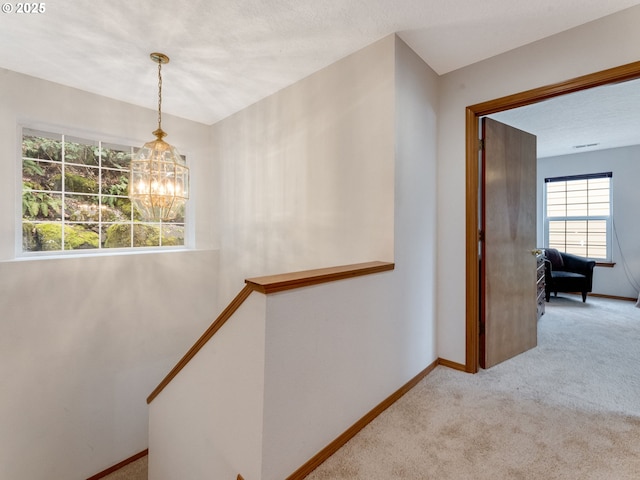 hallway with carpet flooring, an upstairs landing, baseboards, and a chandelier