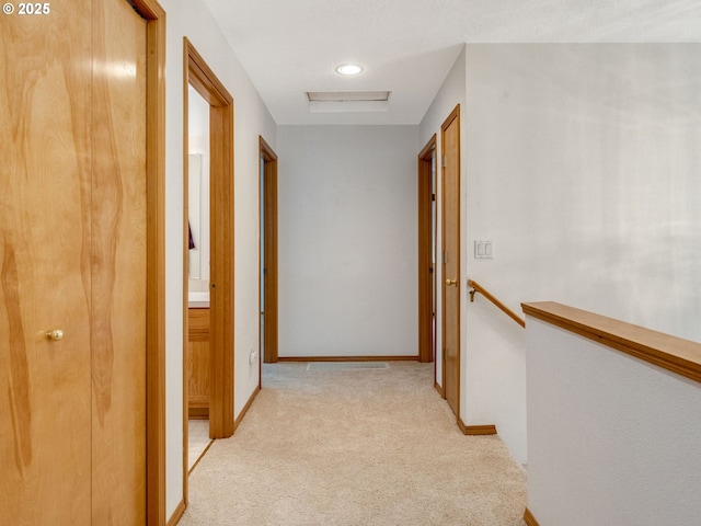 hallway featuring baseboards, light carpet, attic access, and an upstairs landing