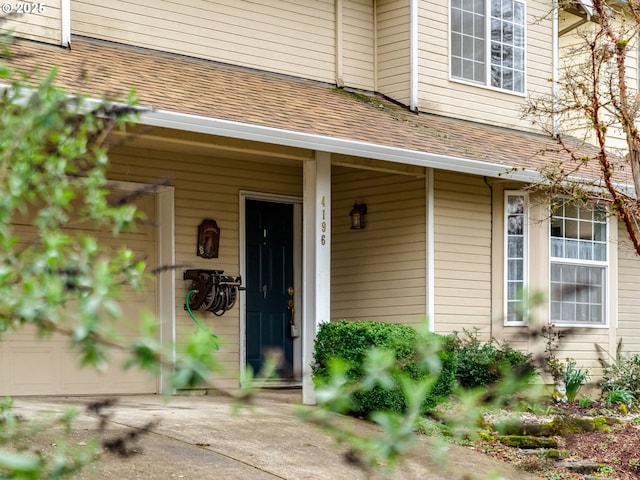 doorway to property featuring covered porch and a shingled roof