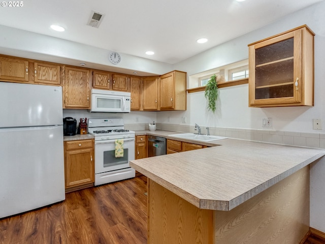 kitchen with dark wood finished floors, light countertops, a peninsula, white appliances, and a sink