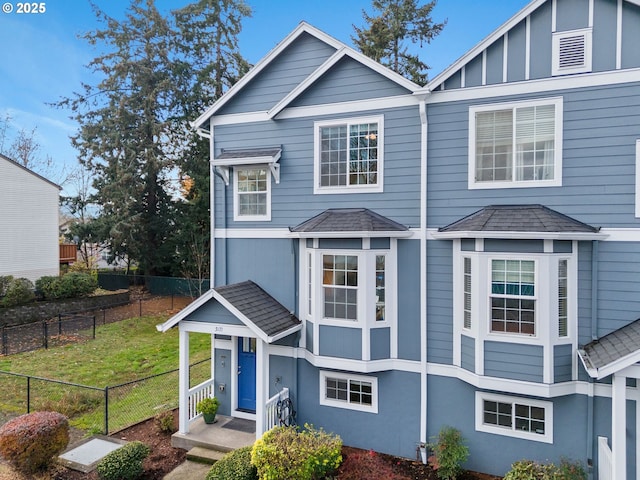 view of front of home with board and batten siding, stucco siding, fence, a front lawn, and a shingled roof