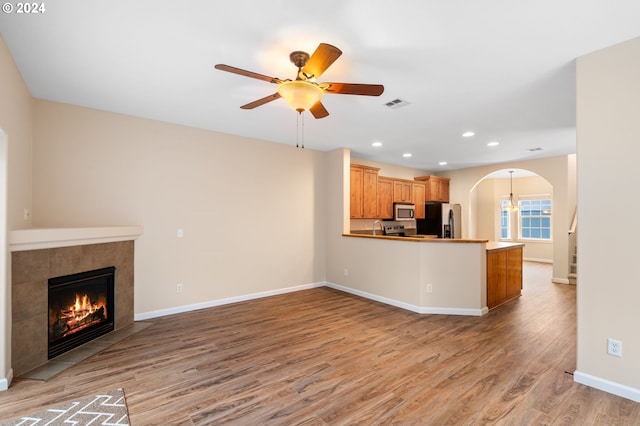 unfurnished living room featuring a tiled fireplace, ceiling fan, and hardwood / wood-style floors