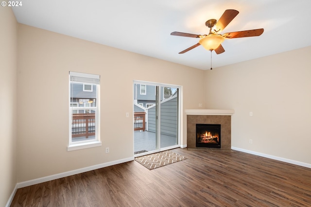 unfurnished living room with baseboards, a ceiling fan, a tile fireplace, and wood finished floors