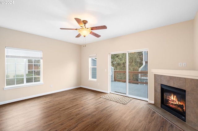 unfurnished living room with plenty of natural light, ceiling fan, dark wood-type flooring, and a tile fireplace