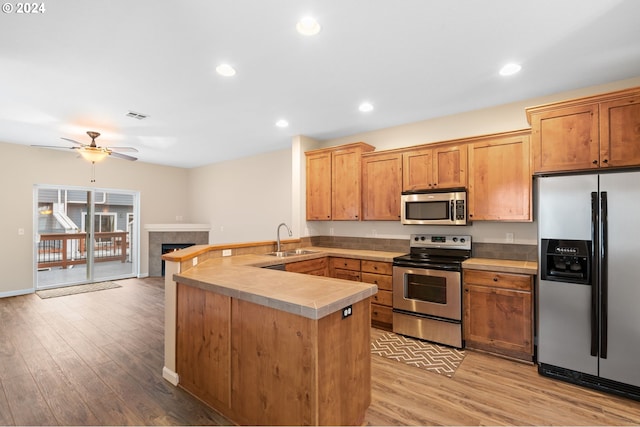 kitchen with ceiling fan, sink, stainless steel appliances, kitchen peninsula, and a fireplace