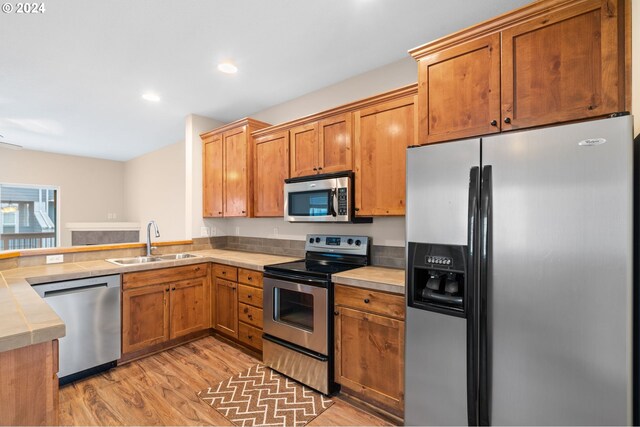 kitchen featuring a peninsula, a sink, stainless steel appliances, light wood finished floors, and tile counters