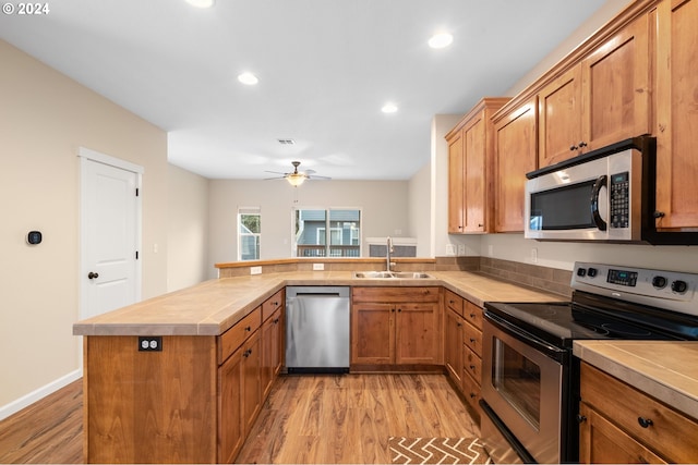 kitchen featuring stainless steel appliances, a peninsula, a sink, light countertops, and light wood finished floors