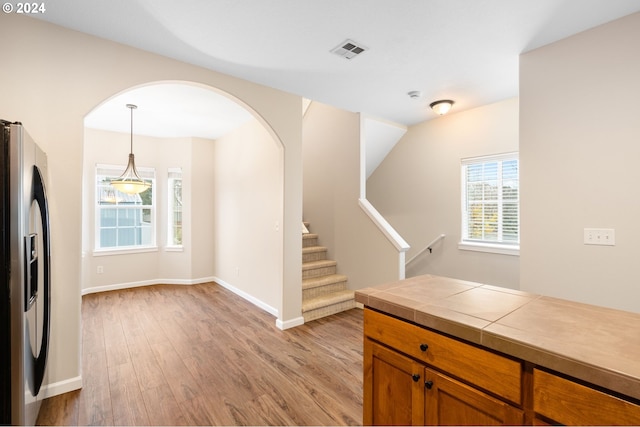 kitchen with tile counters, hanging light fixtures, light hardwood / wood-style flooring, stainless steel refrigerator with ice dispenser, and lofted ceiling