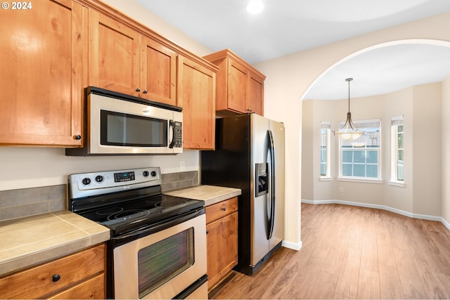 kitchen featuring tile countertops, stainless steel appliances, baseboards, light wood-style floors, and pendant lighting