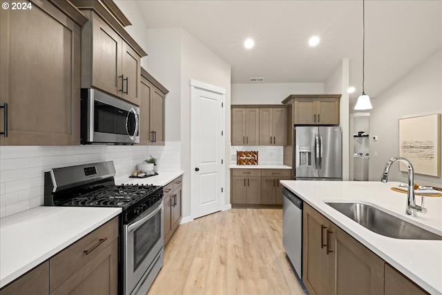 kitchen with sink, tasteful backsplash, hanging light fixtures, light hardwood / wood-style flooring, and stainless steel appliances