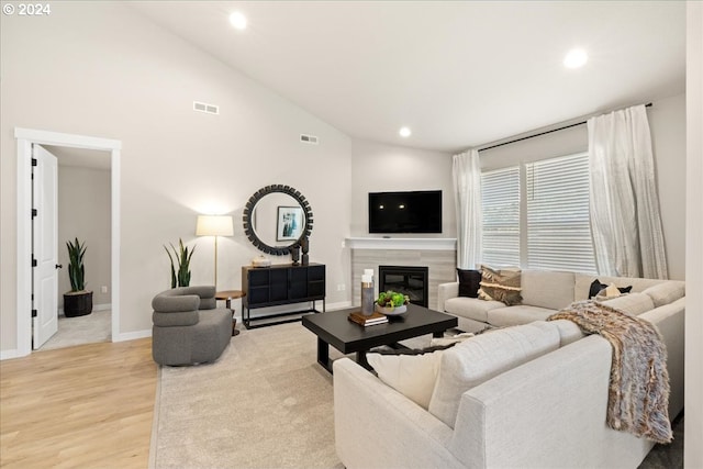 living room with a tiled fireplace, high vaulted ceiling, and light wood-type flooring