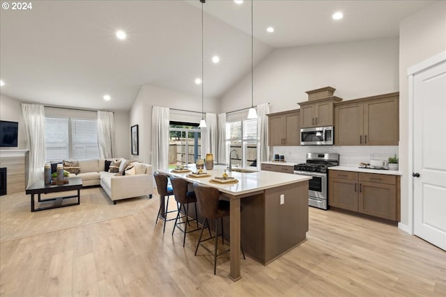 kitchen featuring sink, appliances with stainless steel finishes, a kitchen island with sink, hanging light fixtures, and a kitchen breakfast bar