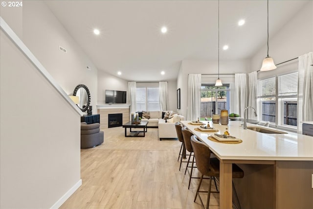 kitchen featuring decorative light fixtures, an island with sink, sink, a kitchen breakfast bar, and light hardwood / wood-style flooring