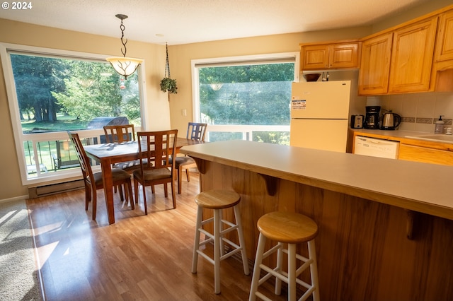 kitchen with white appliances, pendant lighting, a kitchen bar, decorative backsplash, and light wood-type flooring