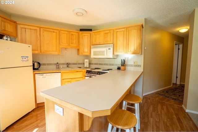 kitchen with sink, white appliances, light hardwood / wood-style floors, light brown cabinetry, and a breakfast bar